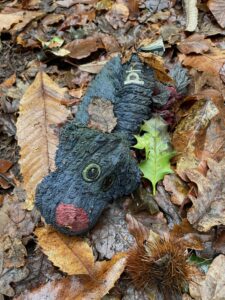 Photo of a dirty, dark blue dog toy with a red nose laying in a bed of brown leaves.