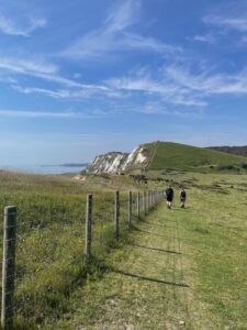 Photo of grassy chalk cliffs, blue skies, and a couple of walkers in the distance.