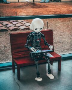 Photo of a robot sitting on a bench reading a book.