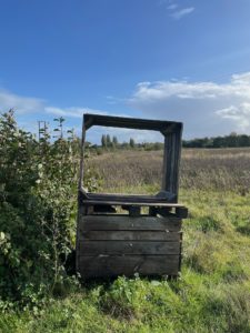 Photo of a large wooden apple crate with the frame of another on top, so it looks like a TV screen. Behind is a field and the blue sky.